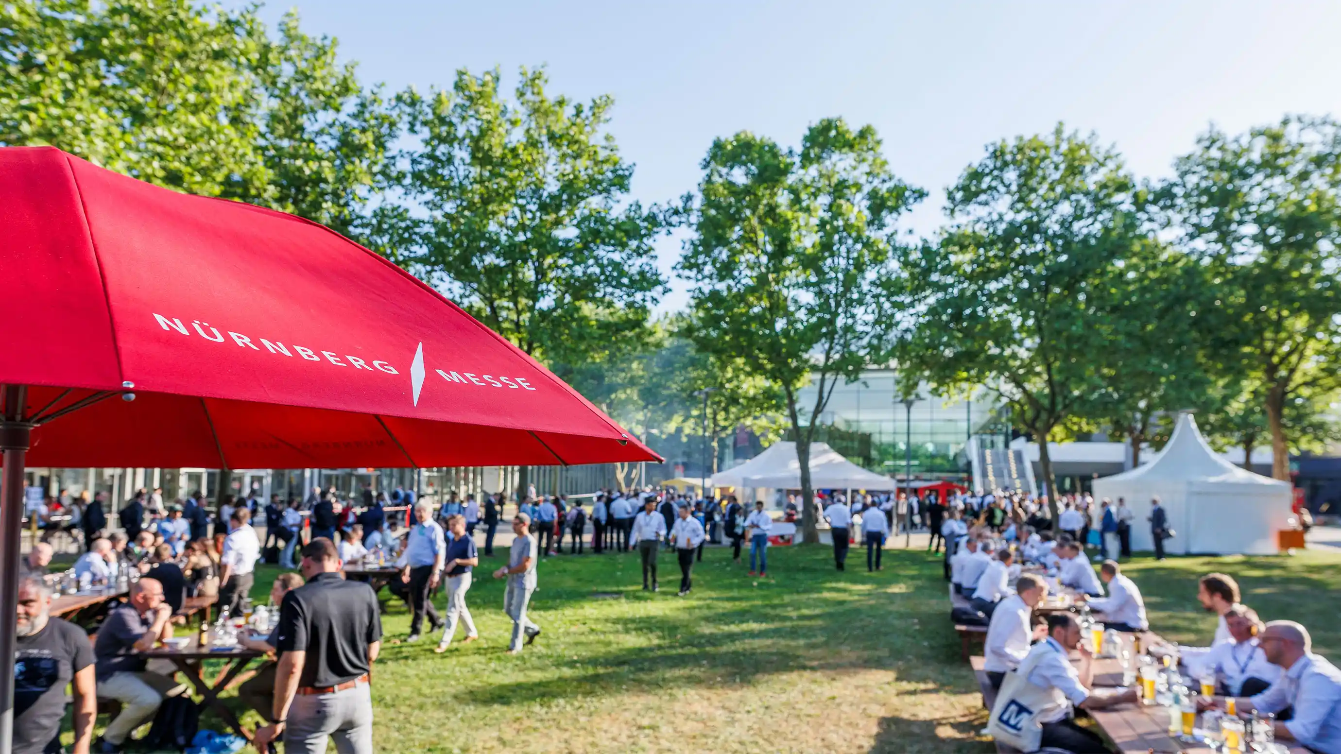 Personen sitzen im Freien auf Bierbänken und trinken und essen.